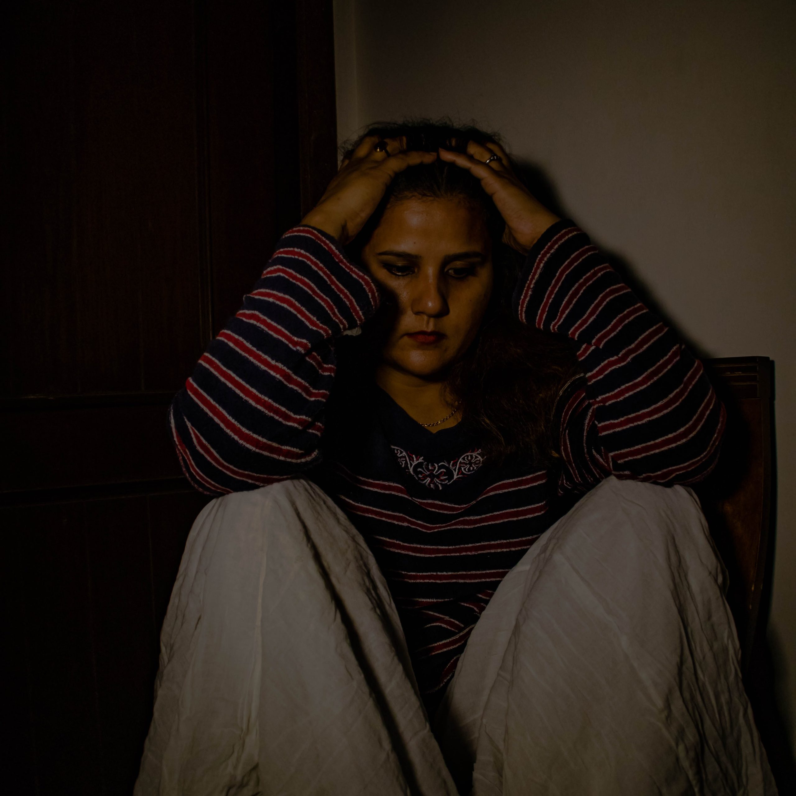 a girl sitting in a dark room with her hands in her hair looking sad