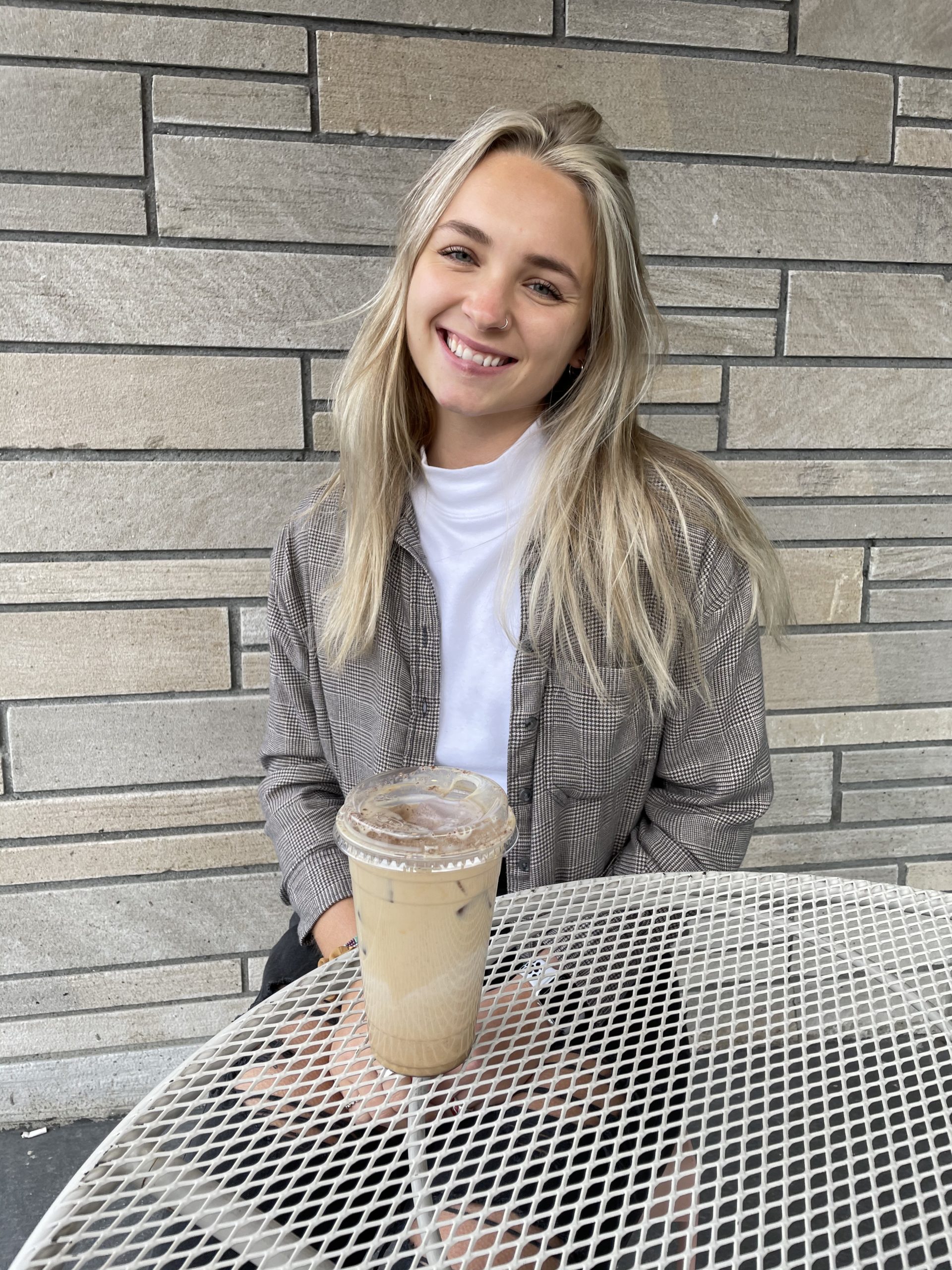 a girl sitting and smiling with an iced coffee in front of her