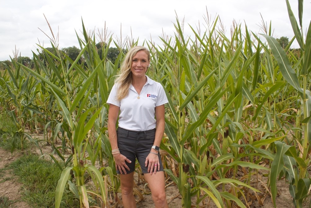 a woman standing in front of a field of corn smiling
