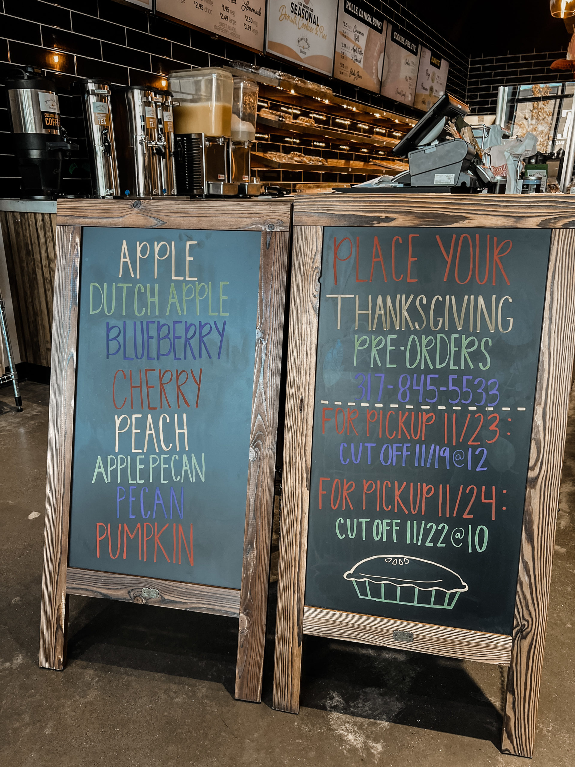 two chalkboard signs. the one on the left reads: apple, dutch apple, blueberry, cherry, peach, apple pecan, pecan, and pumpkin. the one on the right reads: place your thanksgiving pre-orders 3178455533. for pickup 11/23: cut off 11/19 at 12:00. for pickup 11/24: cut off 11/22 at 10:00