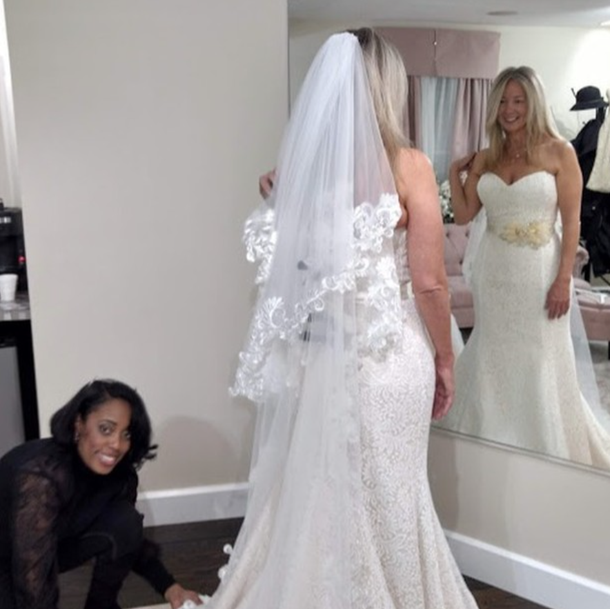 a woman wearing a bridal dress and a worker helping her