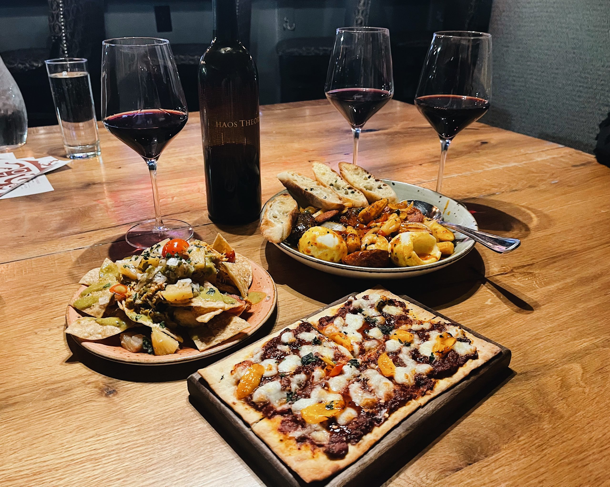 three plates of food on a table with three glasses and a bottle of wine behind them